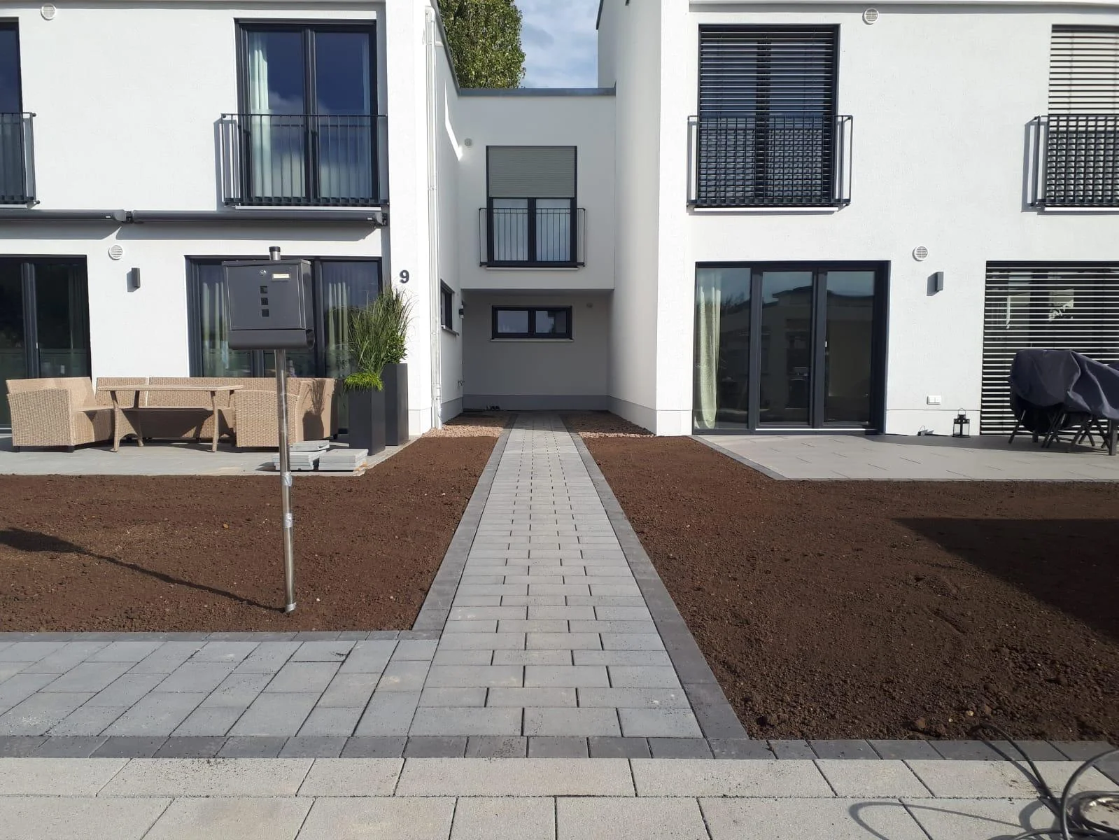 Gepflasterter Zugangsweg zwischen zwei Reihenhaus-Terrassen