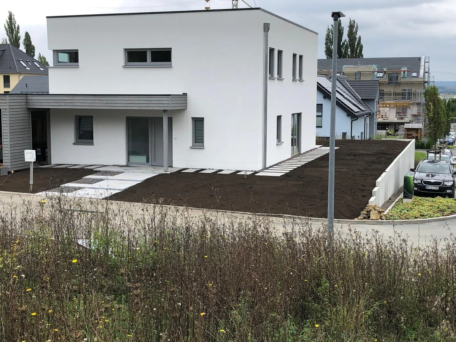 Neu angelegter Vorgarten mit Trittplatten und Stützmauer an einem Neubau