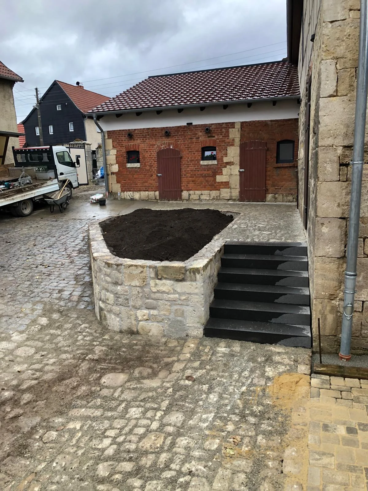 Natursteinmauer als Hochbeet mit Granit-Blockstufen in einem gepflasterten Hof