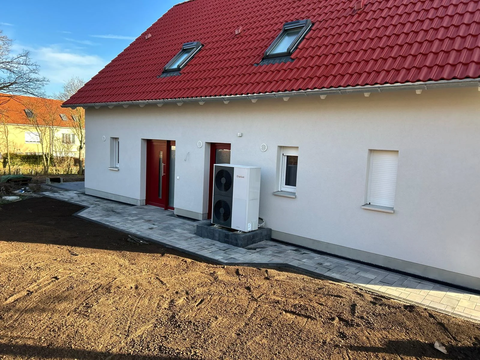 Gepflasterter Weg entlang der Fassade eines Neubaus mit rotem Dach