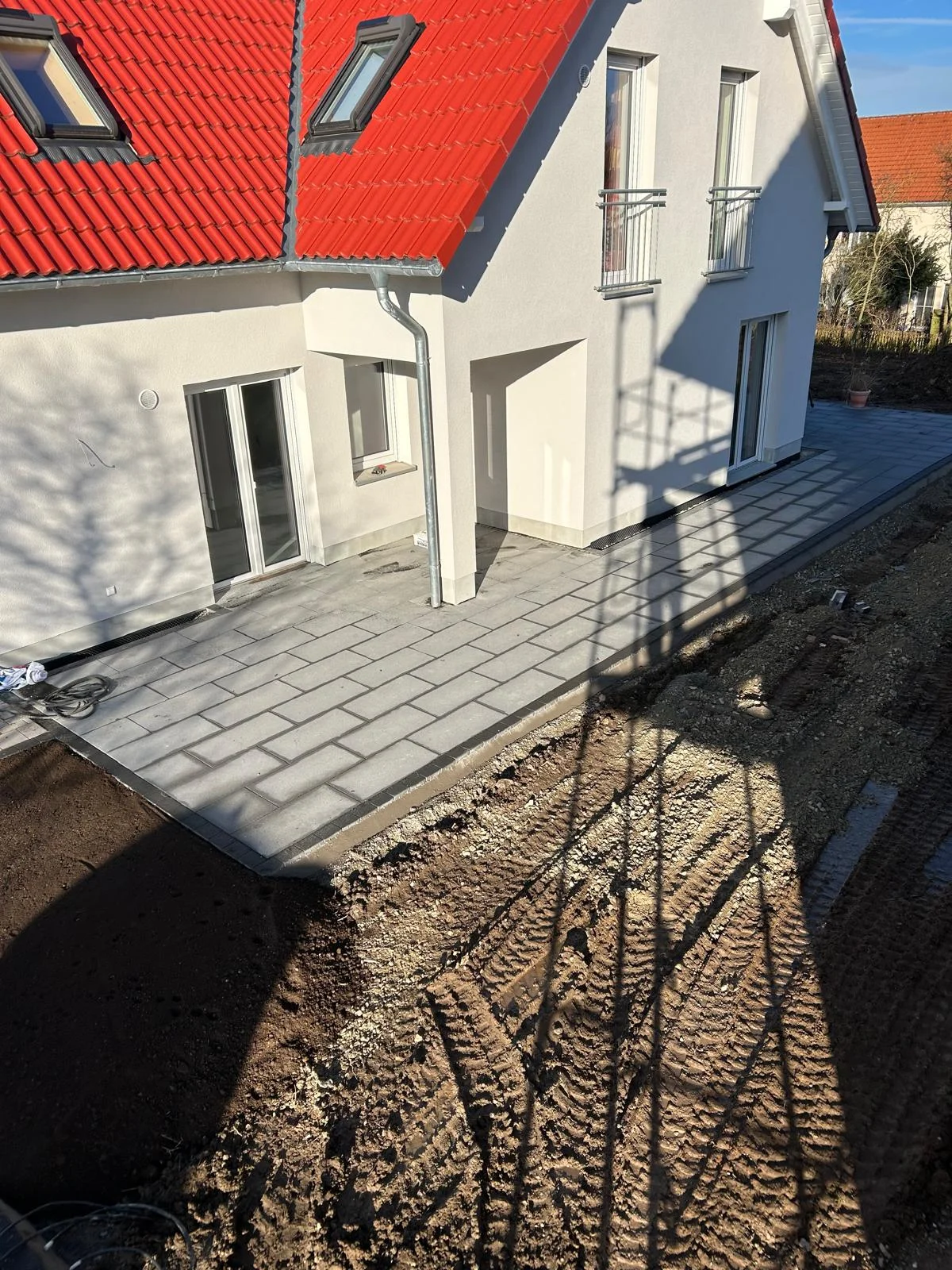 Terrasse aus grauen Betonplatten an einem Neubau mit rotem Ziegeldach