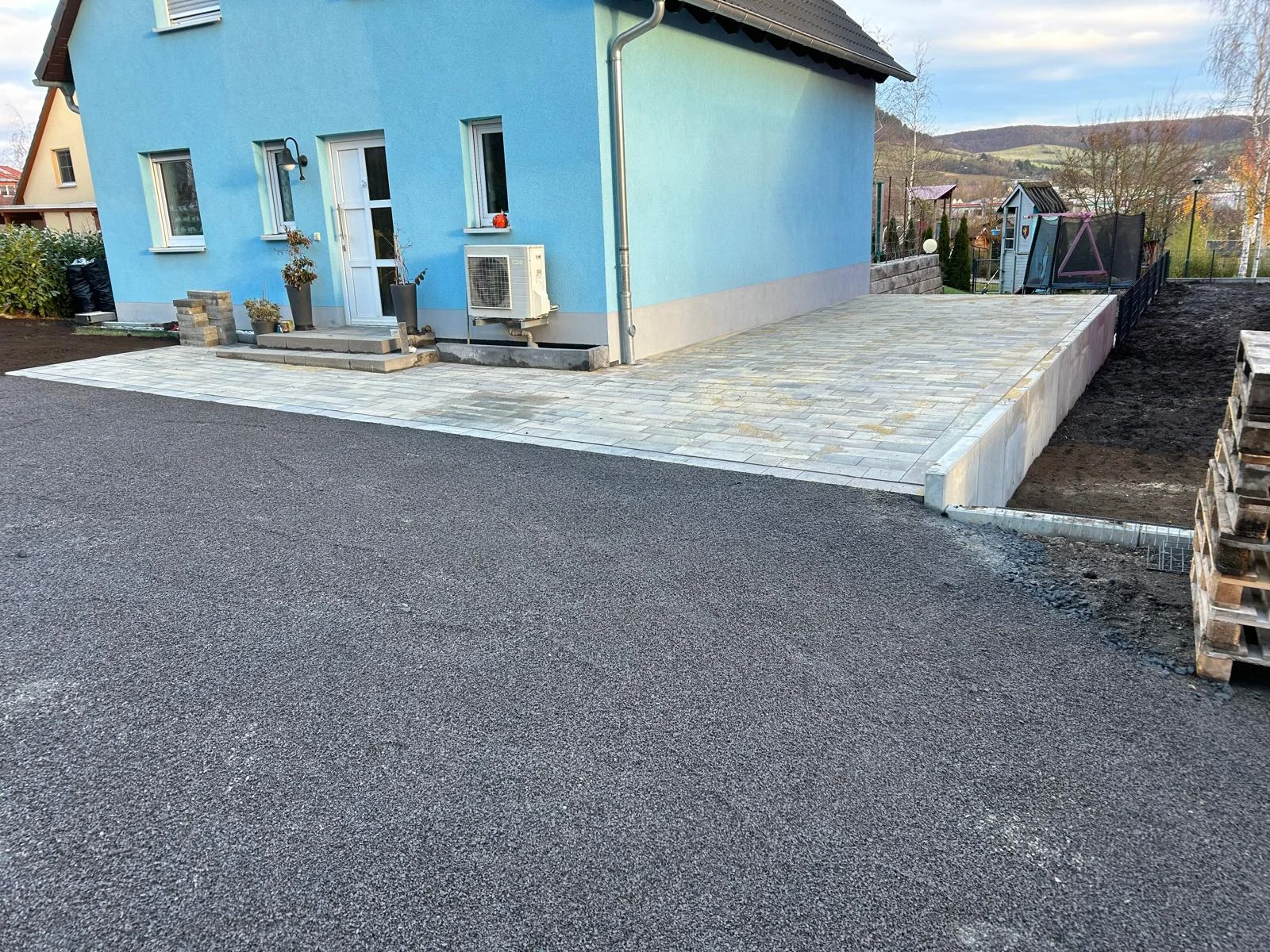 Große gepflasterte Hof- und Terrassenfläche mit Stützmauer an einem Wohnhaus