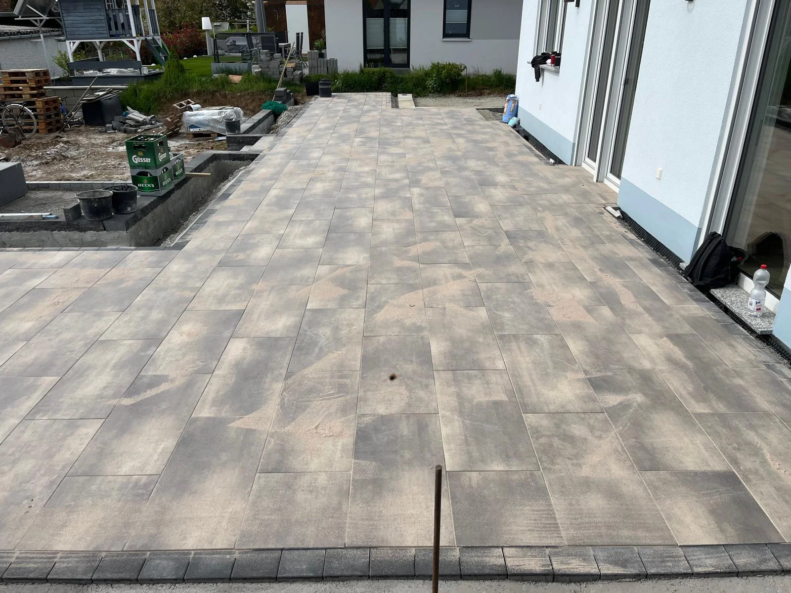Großflächige Terrasse mit anthrazit-beigen Betonplatten entlang der Hausfassade